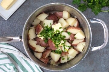 Saucepan with cooked red potatoes, butter, salt, and parsley.