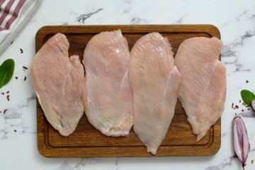 Four Chicken Cutlets on wooden cutting board.