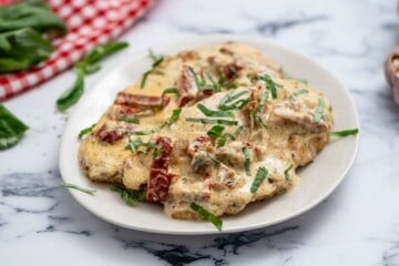 Chicken with sundried tomatoes and parmesan cream sauce dished up on white plate.