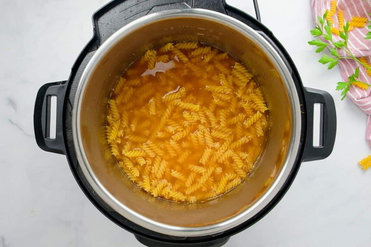 Instant Pot showing rotini noodles covered in seasoned broth inside inner pot.