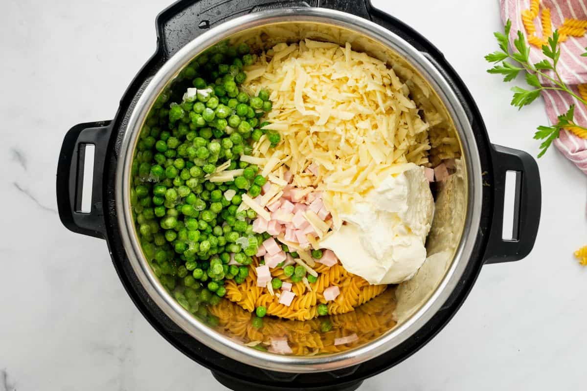 Inner pot with cooked rotini, cheddar cheese, peas, sour cream, and cubed ham.