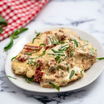 Chicken cutlets on white plate with parmesan cream and sun-dried tomato sauce.