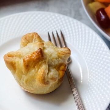 Puff Pastry mini quiche on plate with fork and fruit to side.
