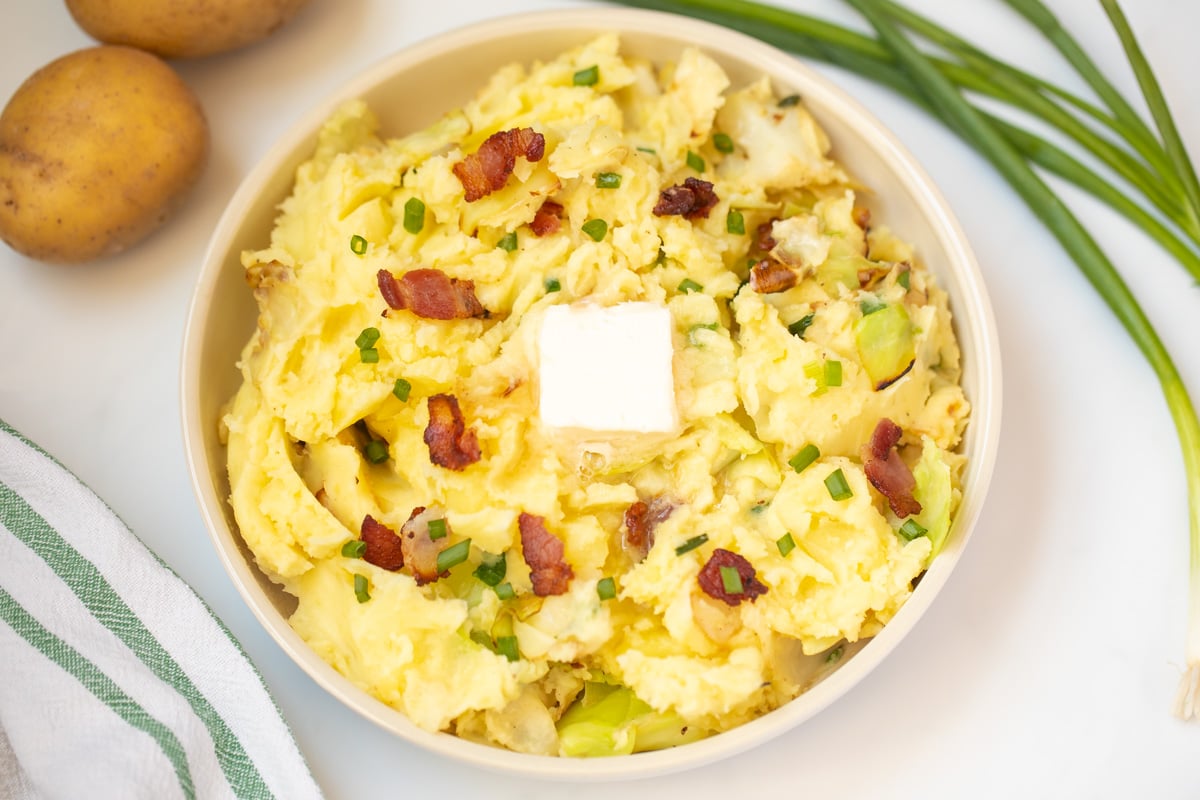 Colcannon in serving dish topped with a pat of butter and bacon.