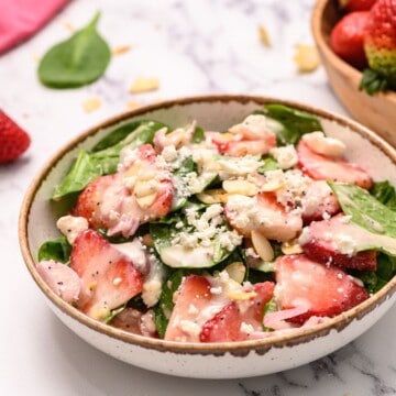 Spinach salad in serving dish topped with strawberies and poppyseed dressing.