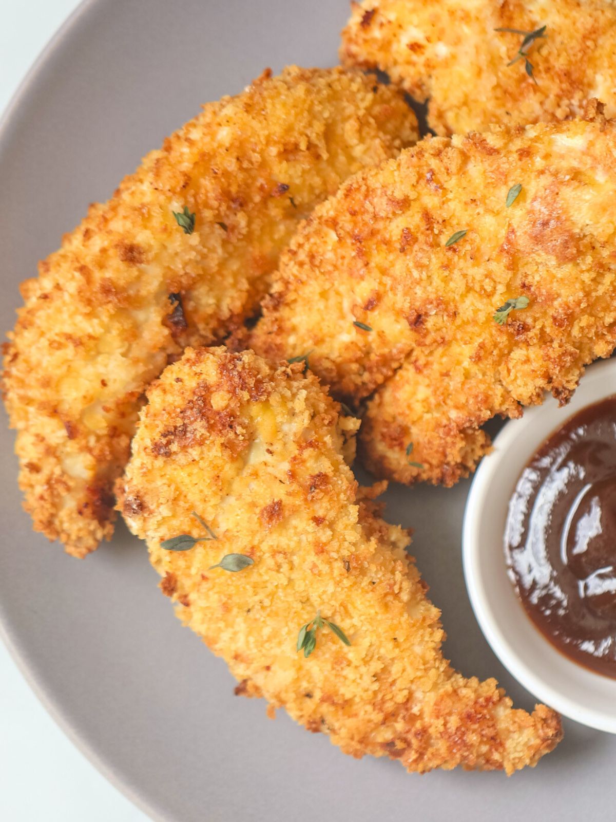 Crispy Air Fryer Chicken Tenders on a gray plate next to BBQ sauce.