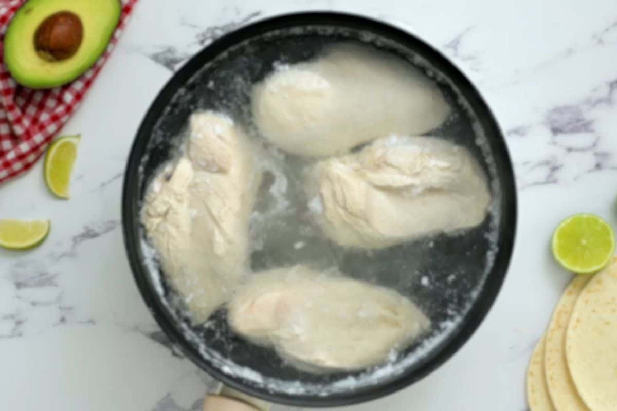 Chicken breasts are poached in water in a small saucepan.