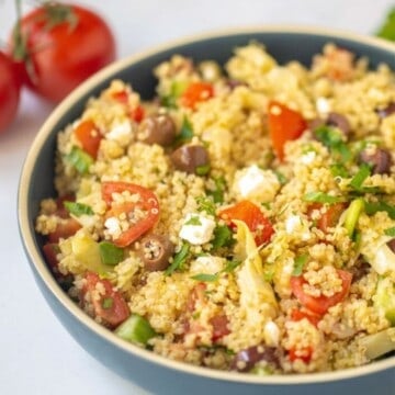 Greek Quinoa Salad served in blue serving dish with tomatoes in background.