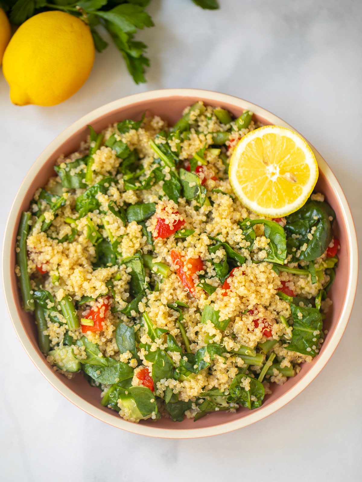 Bowl of quinoa spinach salad with fresh lemon in background.