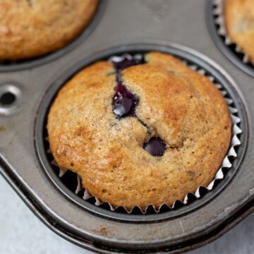 Whole Wheat Blueberry Muffin in muffin tin next to fresh blueberries.