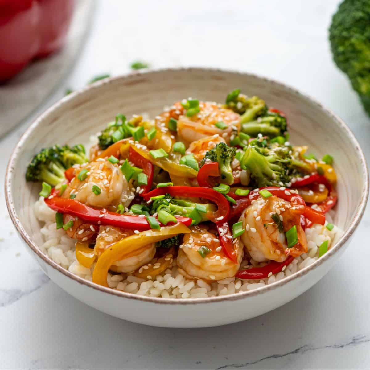 Shrimp stir fry served on top of rice with fresh broccoli in background.