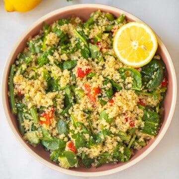 Bowl of quinoa spinach salad with lemon wedges and fresh green beans.