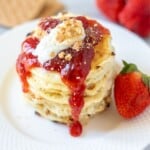 Stack of strawberry cheesecake pancakes topped with strawberry jam and graham crackers.