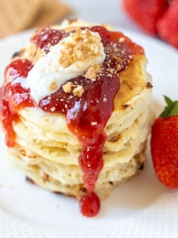 Stack of strawberry cheesecake pancakes topped with strawberry jam and graham crackers.