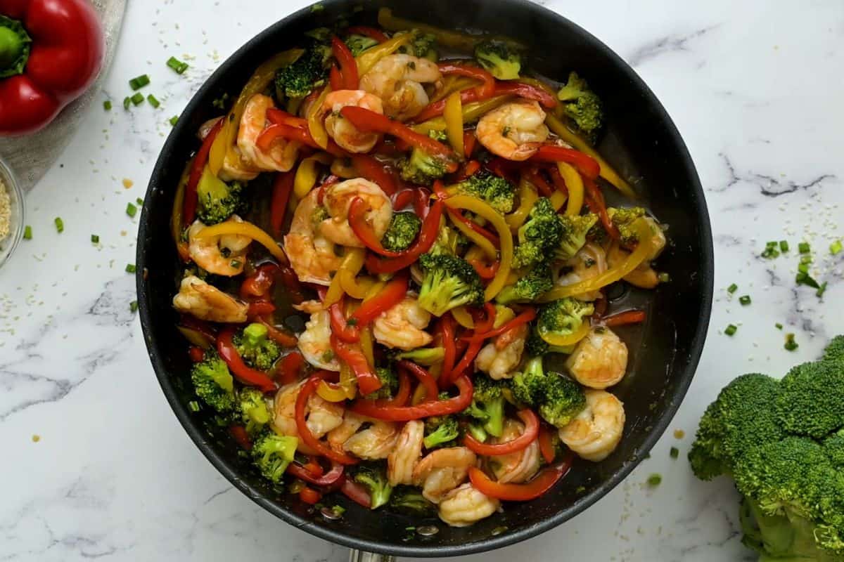 Shrimp and vegetables in saute pan with stir fry sauce.