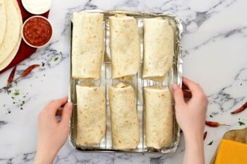 Assembled bean burritos on baking sheet fitted with wire rack.