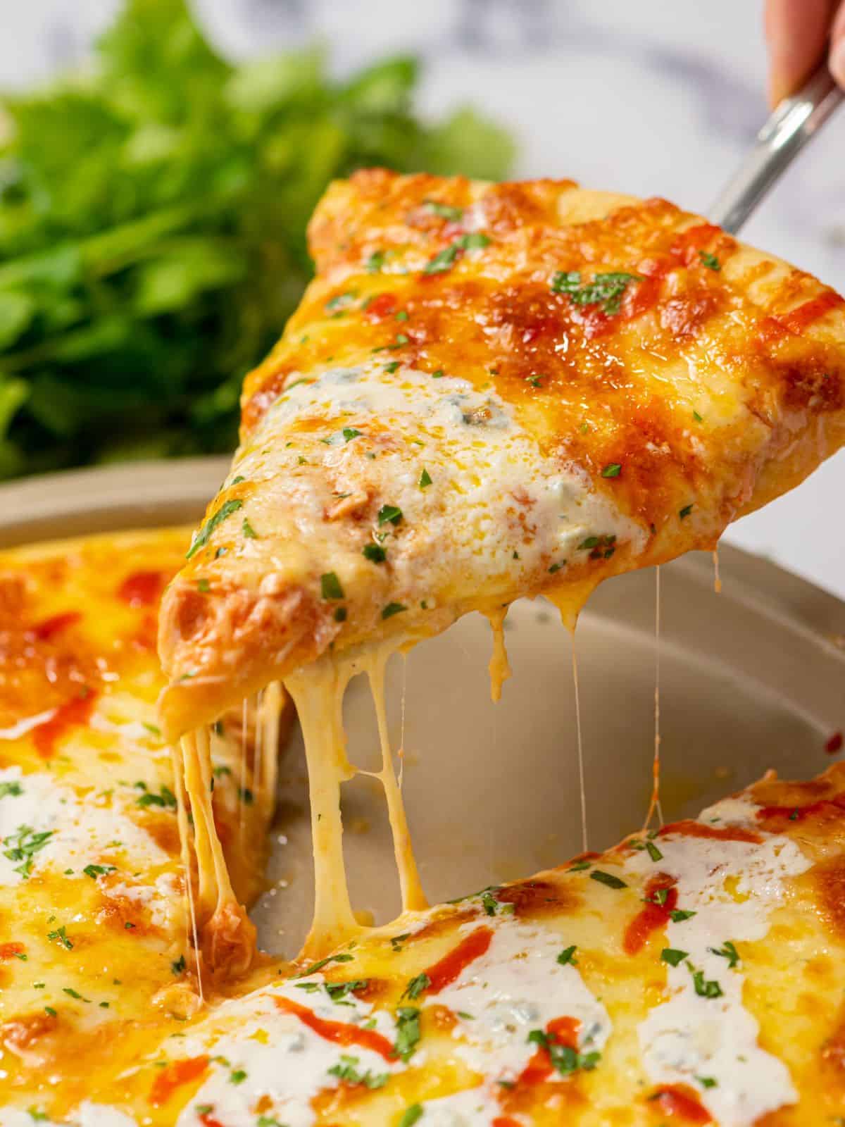 Slice of buffalo chicken pizza being removed from pizza pan, showing cheese pull.