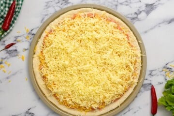Pizza with cheddar and mozzarella cheese over buffalo chicken before baking.