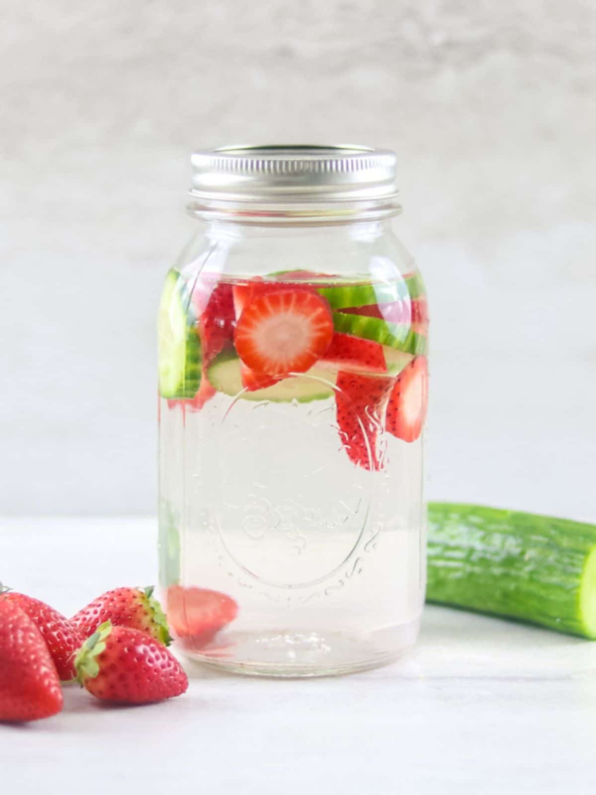 Mason Jar with sliced strawberries and cucumbers and water.