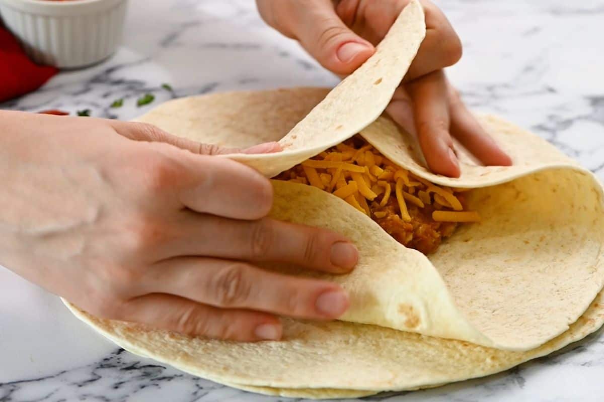 Hands folding in sides of tortilla to cover filling of burrito.