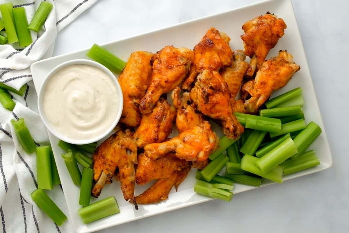 Buffalo Sauce on Buffalo Chicken wings next to ranch and celery.