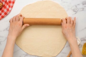 Rolling pin rolling homemade pizza dough into circle.