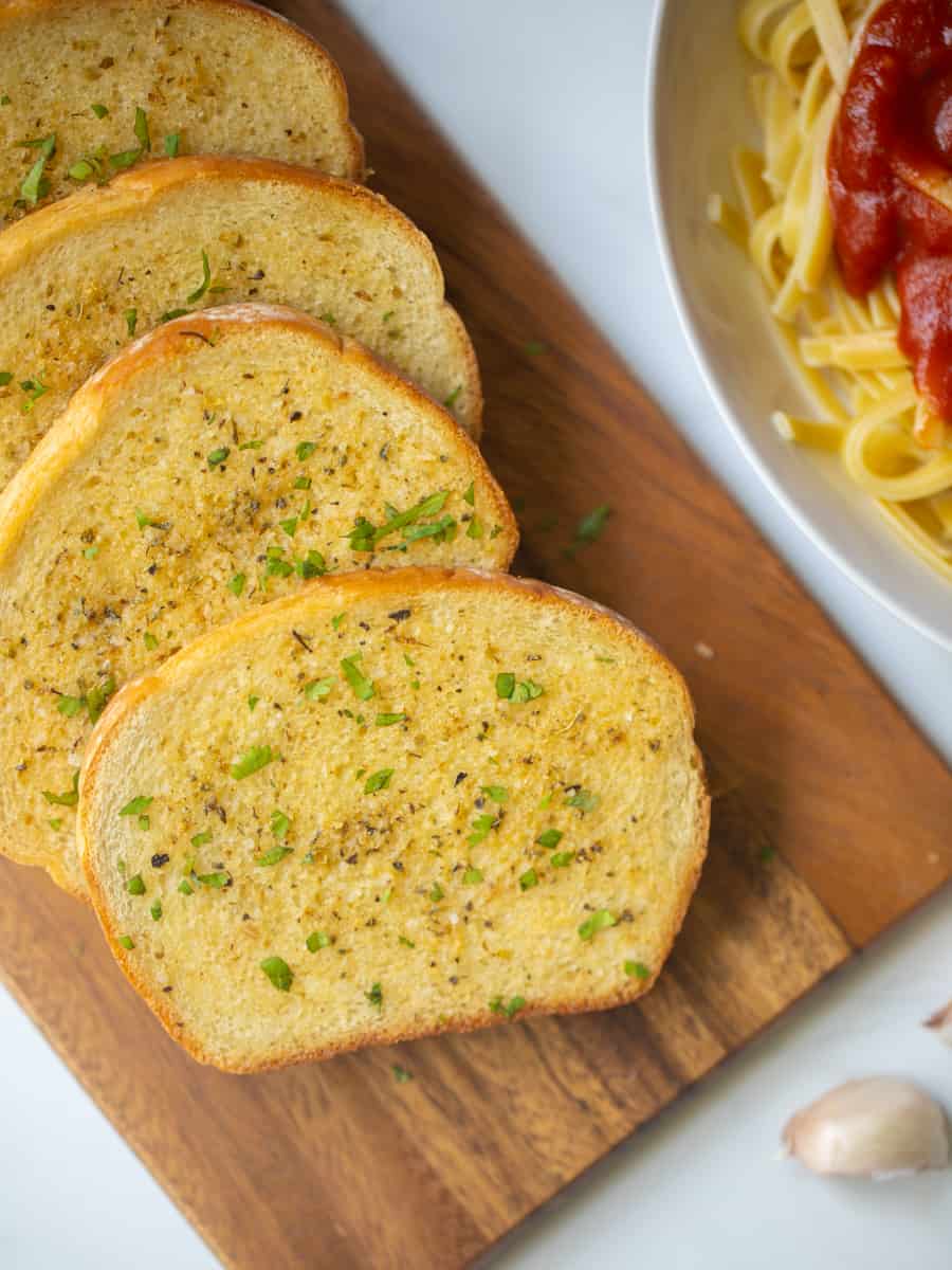 Toasted garlic bread on cutting board topped with fresh parsley.