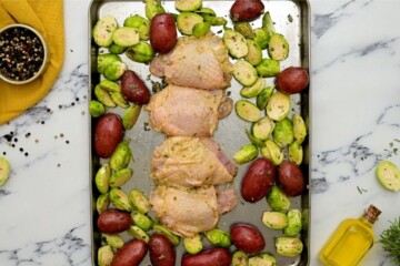 Seasoned Chicken Thighs, potatoes, and brussels sprouts spread out on sheet pan.