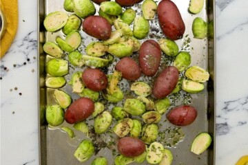 Potatoes and brussels sprouts tossed with olive oil and seasonings on sheet pan.