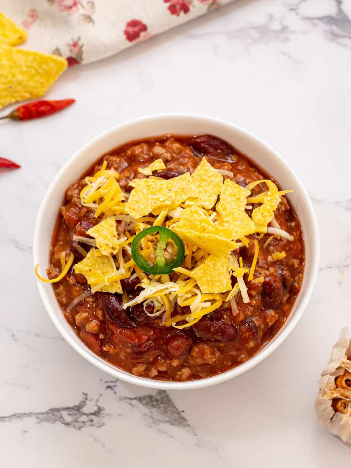 Bowl of crockpot chili topped with corn chips, shredded cheese, and jalapeno.