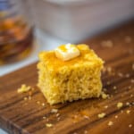 Slice of cornbread topped with a pat of butter and drizzle of honey on cutting board.