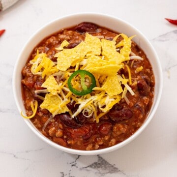 Bowl of crockpot chili topped with corn chips, shredded cheese, and jalapeno.