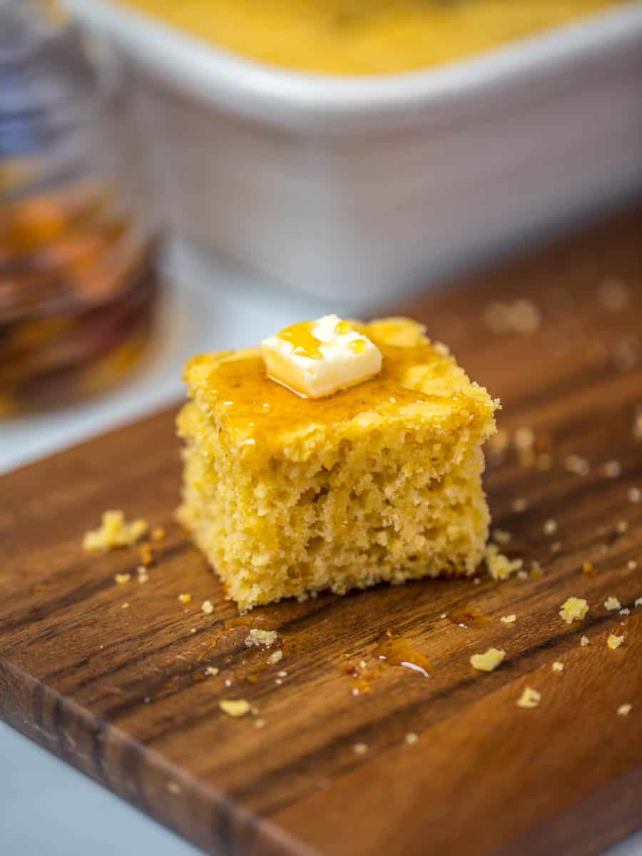 Slice of cornbread on cutting board with dab of butter drizzled with honey.