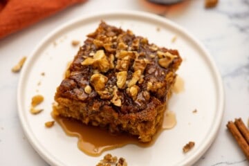 Slice of baked pumpkin oatmeal on plate topped with maple syrup and nuts.