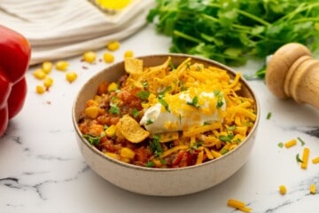 Bowl of sweet potato quinoa chili topped with sour cream and corn chips.