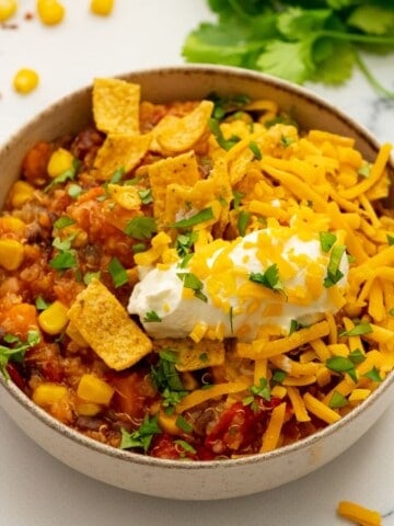 Bowl of sweet potato quinoa chili topped with sour cream and corn chips.