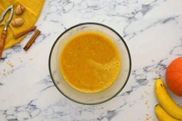Pumpkin puree, eggs, banana, and maple syrup mixed together in mixing bowl.