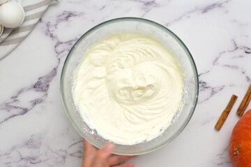 Cream cheese frosting after powdered sugar mixed in in clear mixing bowl.