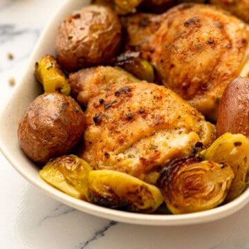 Sheet pan chicken thighs with potatoes and vegetables on white dish.
