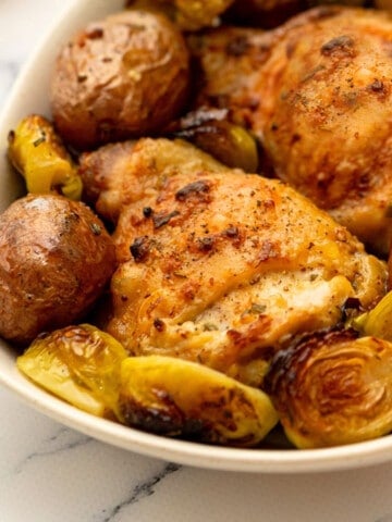 Sheet pan chicken thighs with potatoes and vegetables on white dish.
