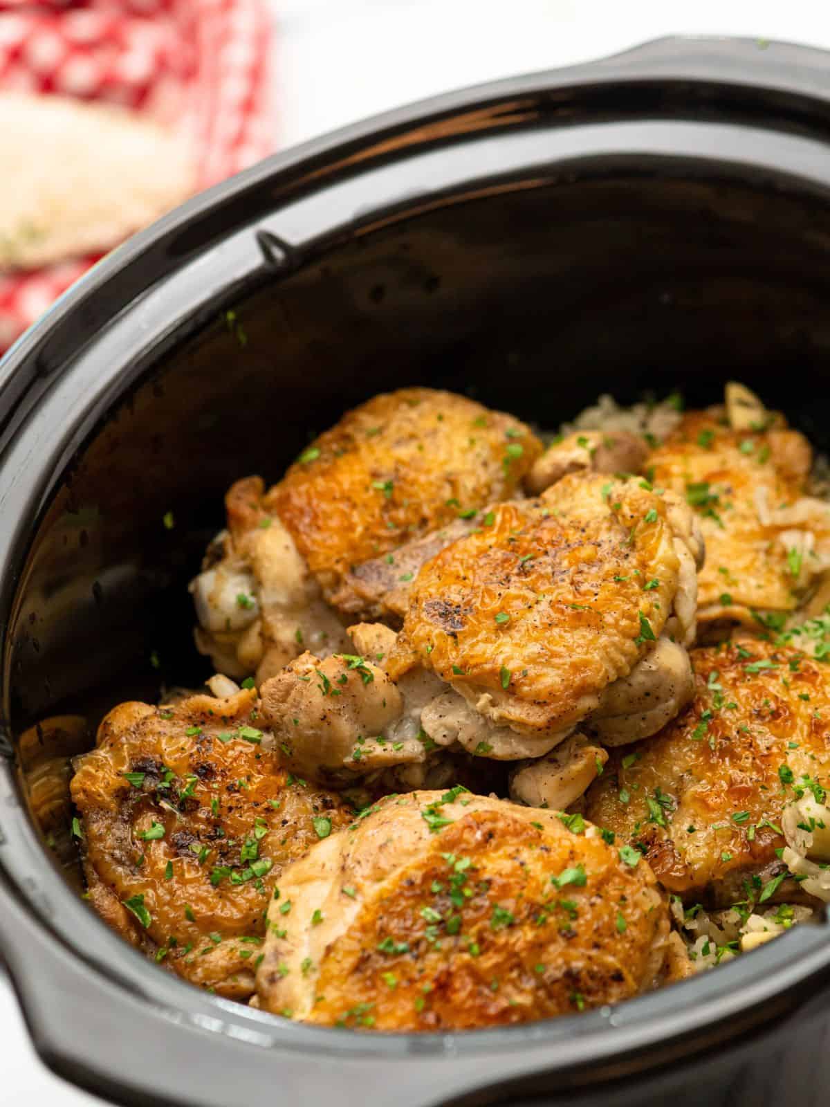 Crockpot with cooked rice and seared chicken thighs.