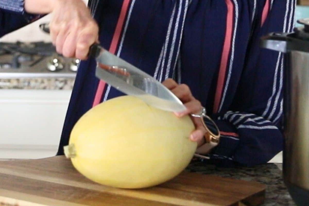 Knife running widthwise across a spaghetti squash to cut in half.