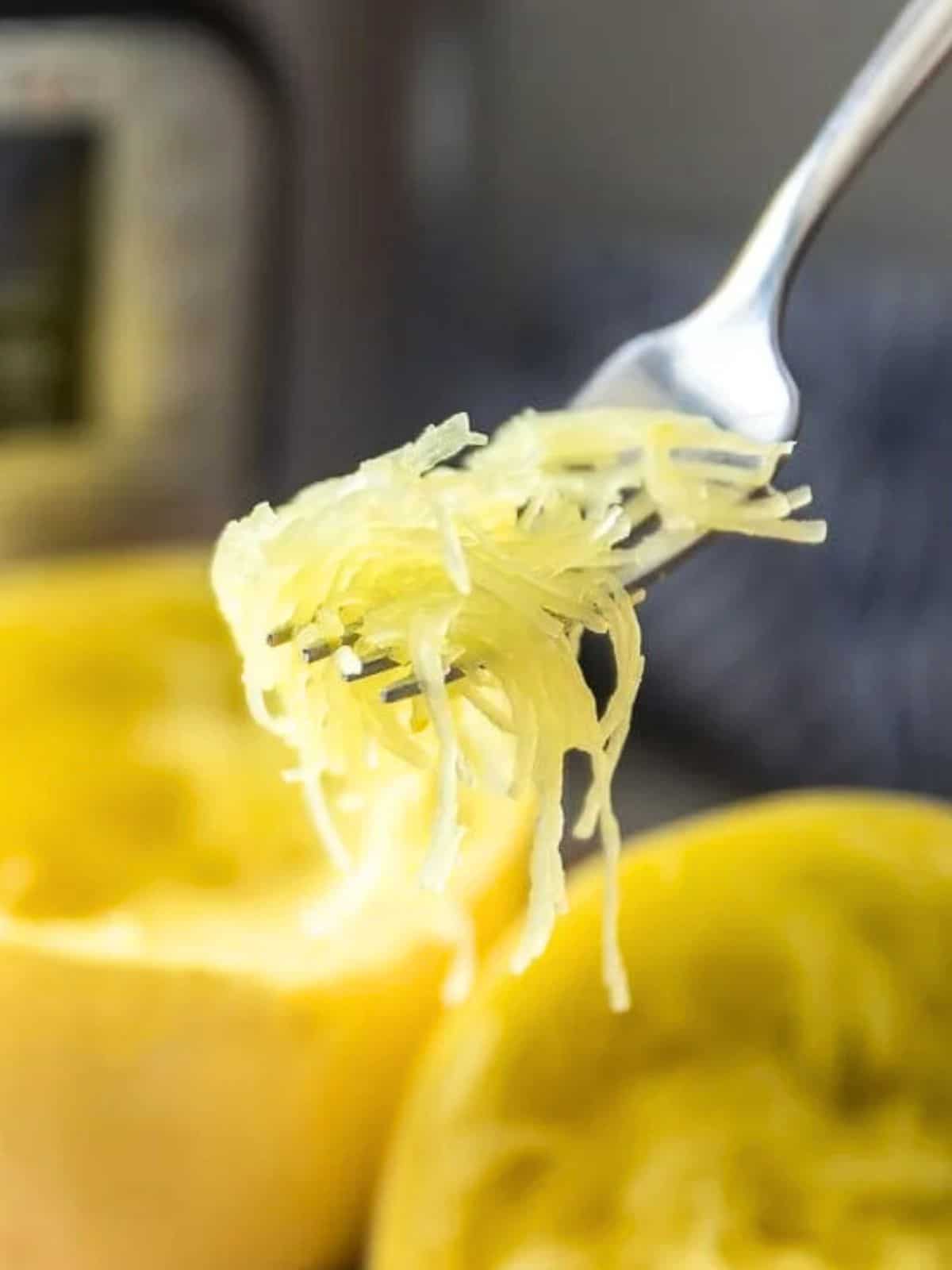 Fork scooping out perfectly cooked spaghetti squash from squash next to Instant Pot.