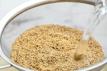 Quinoa in mesh strainer with water running over it.