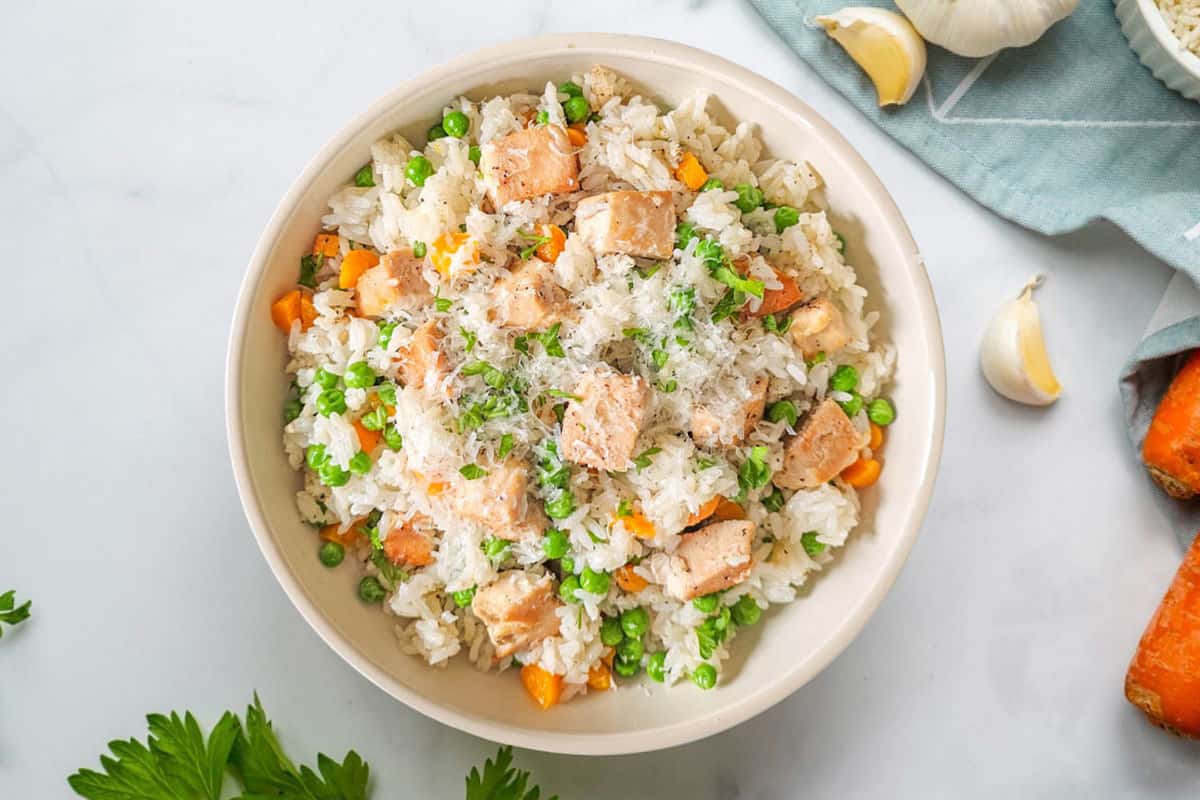 Easy Instant Pot Meals Bowl of Instant Pot Chicken and rice plated in cream bowl with garlic cloves in the background.