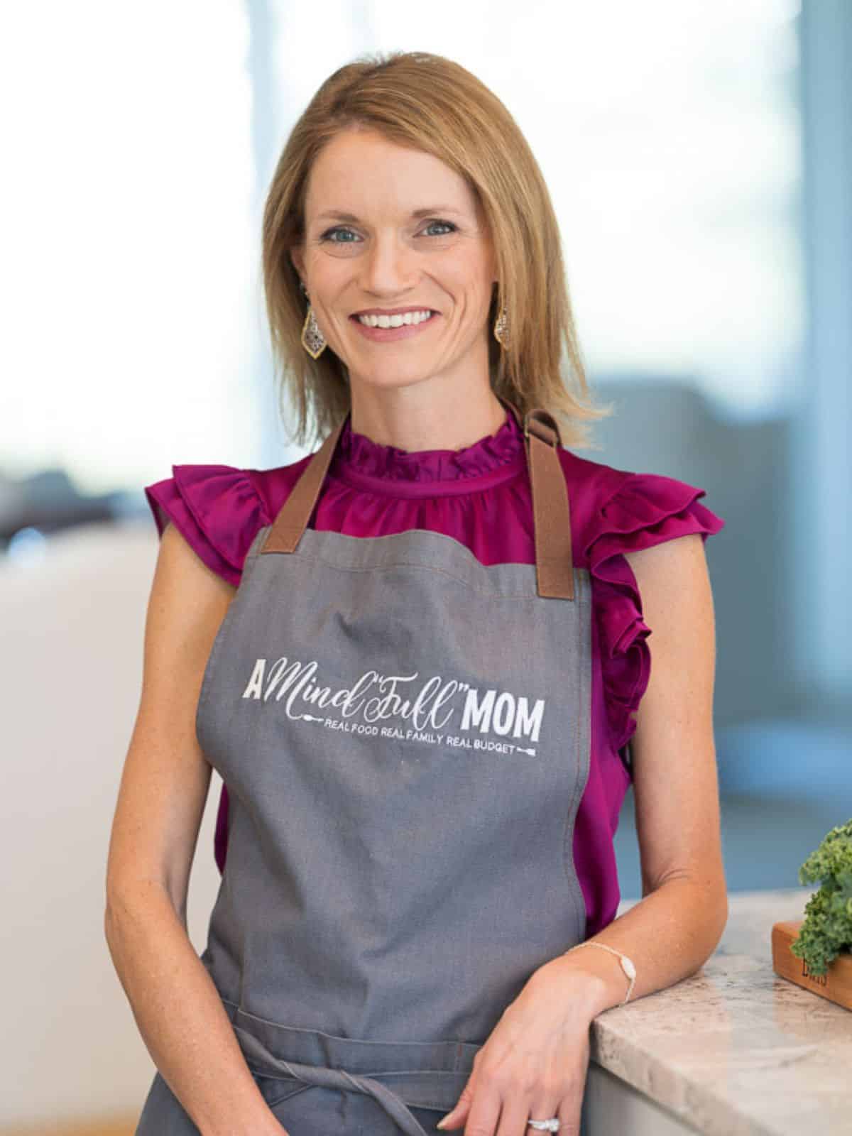 Kristen wearing an apron that reads. A Mind Full Mom Real food real families real budget.