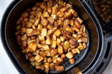 Air fried cubed potatoes in air fryer basket.