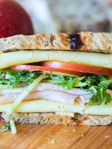 Turkey apple sandwich with white cheddar and kale salad on cutting board