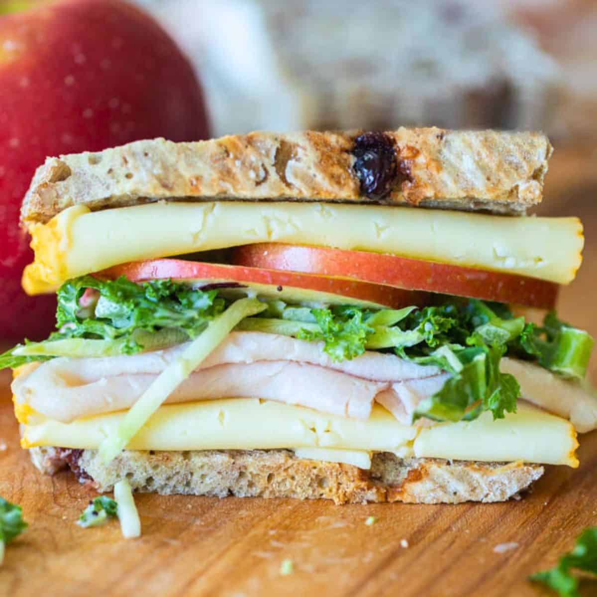 Turkey apple sandwich with white cheddar and kale salad on cutting board