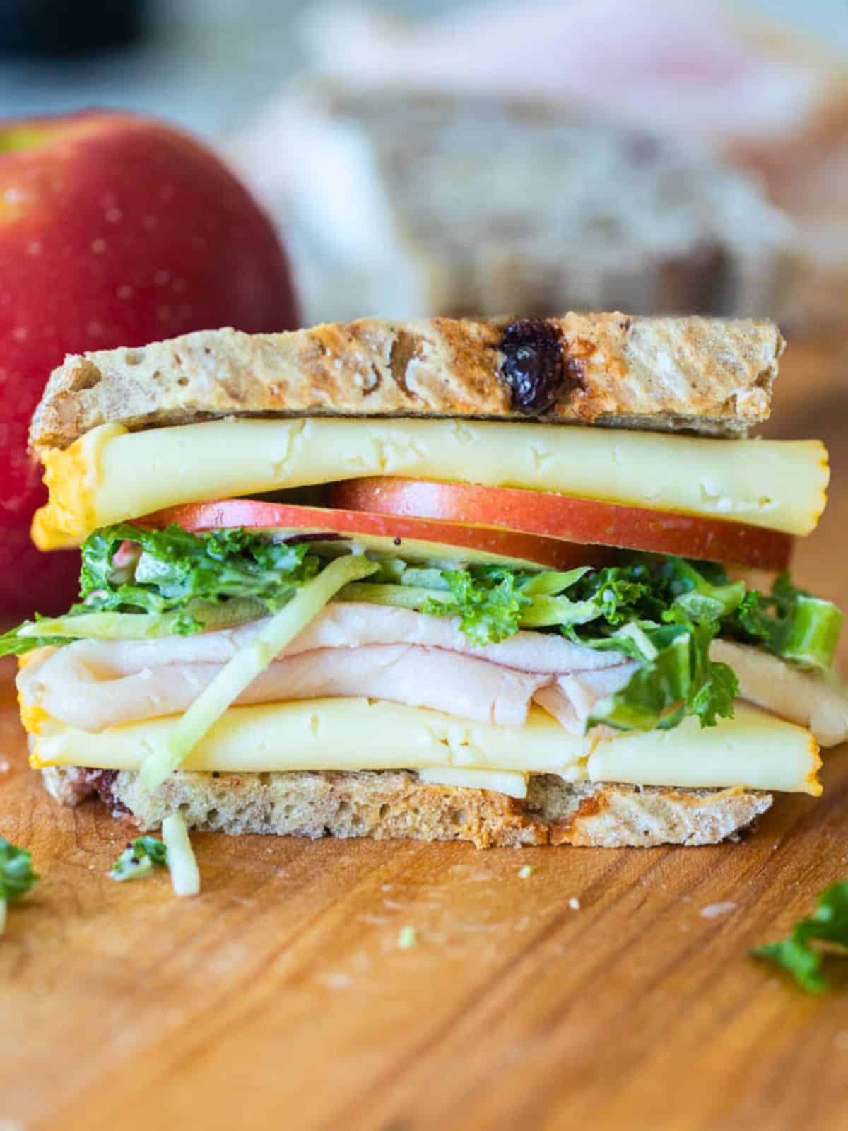 Turkey apple sandwich with white cheddar and kale salad on cutting board.